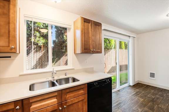 A kitchen with a black dishwasher and wooden cabinets.