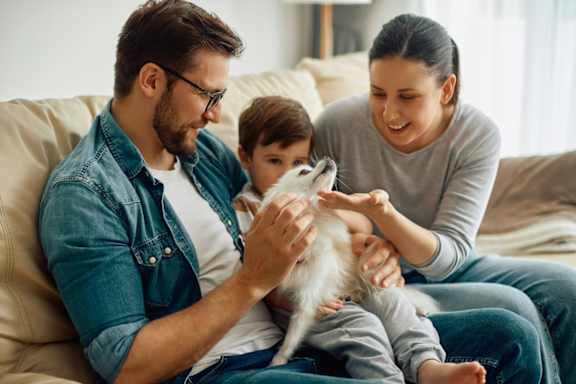 A family of three is sitting on a beige couch with a white cat.