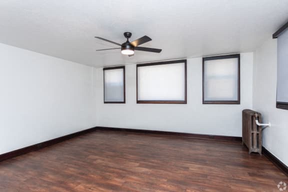 an empty living room with a ceiling fan and three windows