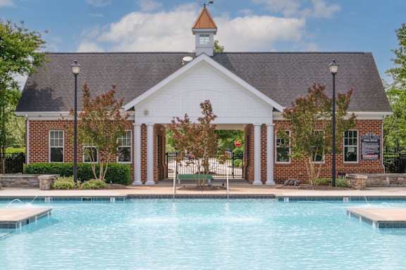 A pool in front of a building with a clock tower. at Fenwyck Manor Apartments