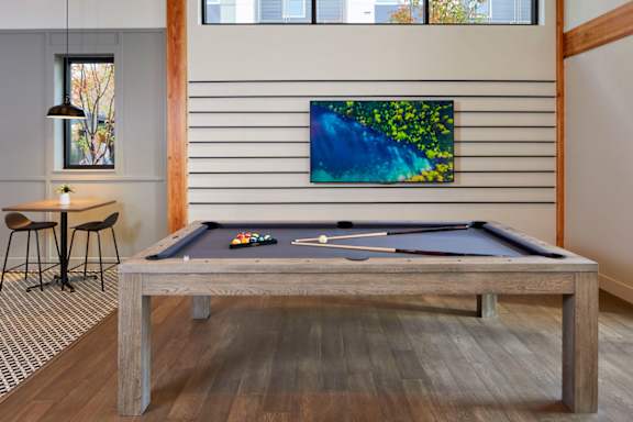 A pool table with a green cloth and balls is in the middle of a room with a painting hanging on the wall.