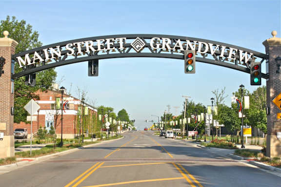 A street sign for Main Street Grandview is above a road with a green light.