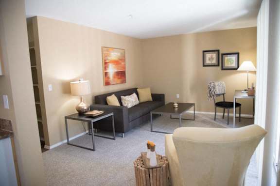 A living room with a black couch, a glass table, and a white chair.