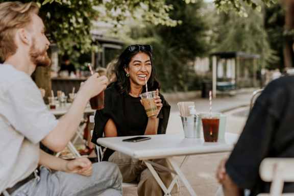 People Smiling while Sitting at Table Outside and Drinking Coffee