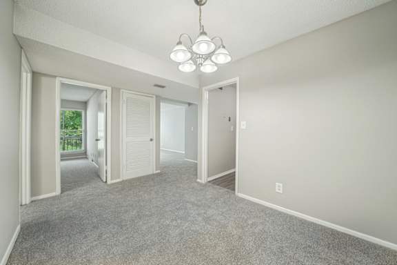 A spacious room with a grey carpet and a chandelier hanging from the ceiling.