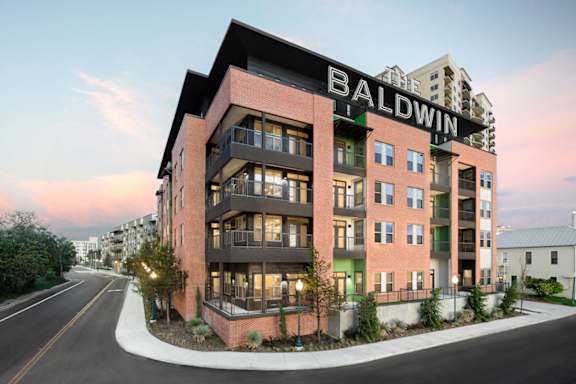 Exterior view of a modern apartment building with balconies, large windows, and street-facing landscaping.