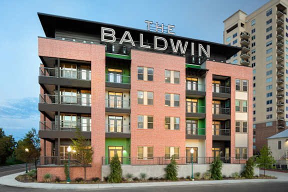 Exterior view of a modern apartment building with balconies, large windows, and street-facing landscaping