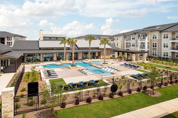 Aerial view of a luxury community pool featuring in-water lounge seating, beautifully landscaped grounds, and modern amenities.