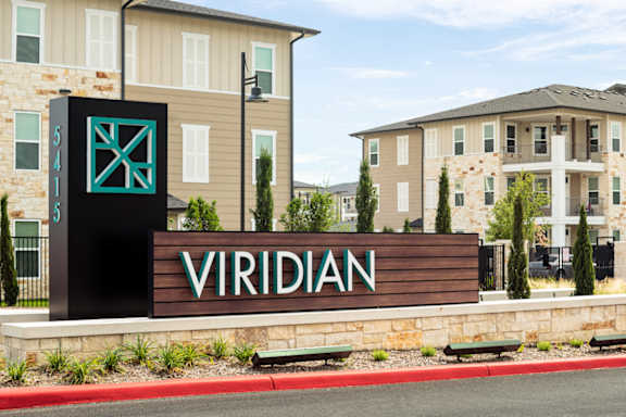 Modern apartment community entrance sign surrounded by landscaped grounds and upscale residential buildings.