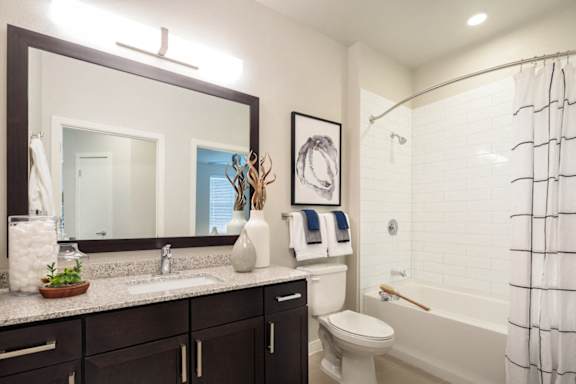 Modern bathroom featuring a spacious vanity, granite-style countertops, and a sleek tub-shower combination.