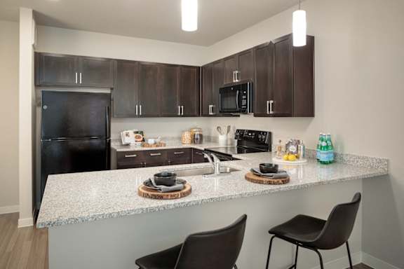 Modern kitchen featuring dark cabinetry, granite-style countertops, and convenient bar seating for casual dining.