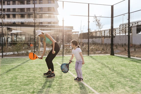 a woman and a child holding tennis rackets on a tennis court