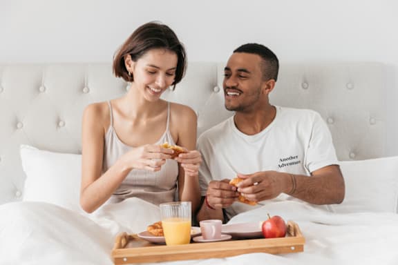a man and a woman sitting in bed eating breakfast