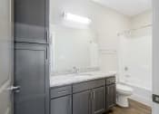 Thumbnail 8 of 8 - a bathroom with a granite countertop sink and a toilet, a tall storage cabinet, and a tub shower