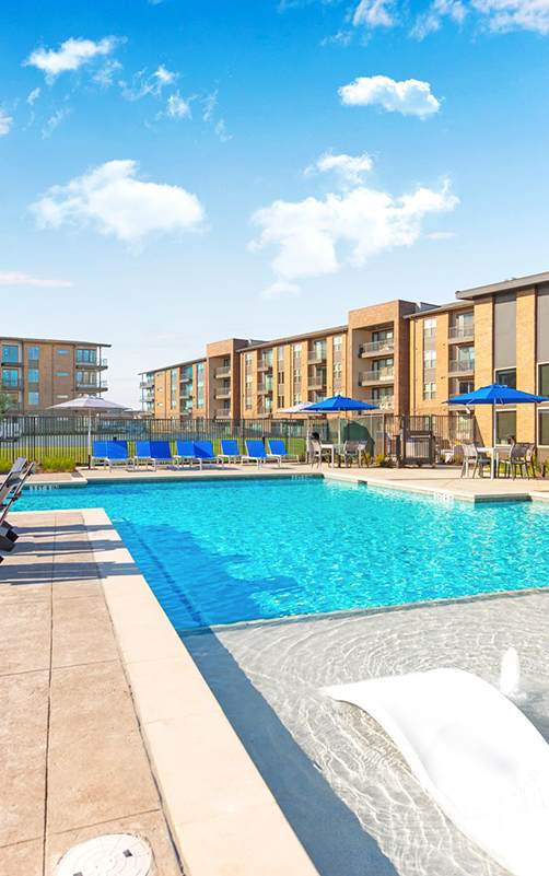 A swimming pool with sun loungers and apartment buildings in the background.