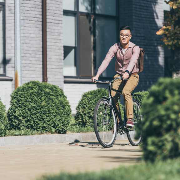 : A man in a pink shirt and khaki pants is riding a bicycle on a sidewalk.