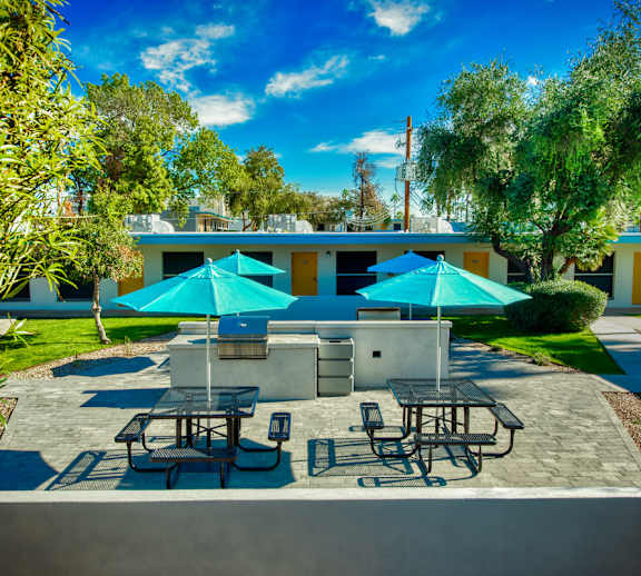 A patio with tables and chairs under blue umbrellas. at The Link Apartments, Mesa, Arizona