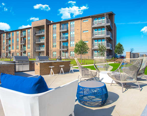 A modern outdoor seating area with white chairs and a blue cushion is set against a backdrop of apartment buildings.