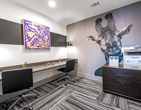 A room with a giraffe mural on the wall and a black chair in front of a desk.