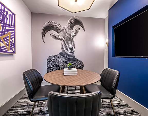 A conference room with a table, chairs, and a painting of a ram on the wall.
