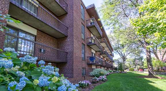 A tall apartment building with balconies and trees in the foreground.