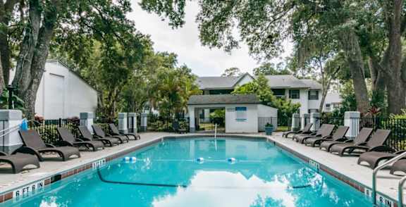 A pool surrounded by trees and chairs.