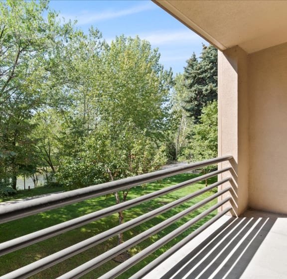 A balcony with a metal railing overlooks a lush green forest. at River Walk Apartments, Boise, ID, 83702