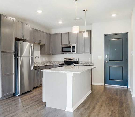 an open kitchen with stainless steel appliances, grey cabinets, and granite counter tops