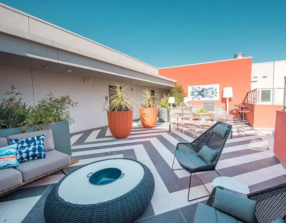 A patio with a couch, chairs, and a table with a blue pot on it.