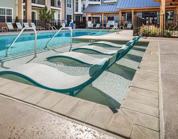 a swimming pool with four chaise lounges and a building in the background