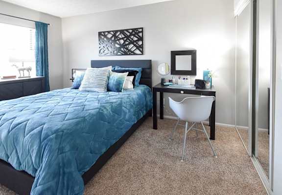 A bedroom with a blue bedspread and a white chair.