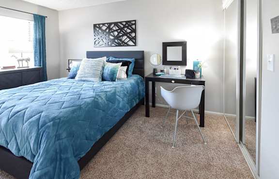 A bedroom with a blue bedspread and a white chair.