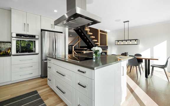 a white kitchen with a large island and a stainless steel refrigerator