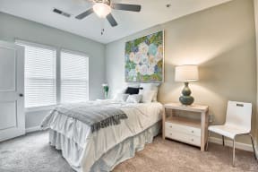 A bedroom with a bed, nightstand, chair, and a painting on the wall.