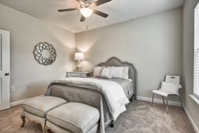 A bedroom with a bed, chair, and ceiling fan.