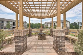 A wooden pergola with benches and a fire pit in the middle of a brick patio.
