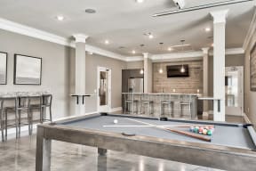 A pool table is in the middle of a room with a bar and a TV.