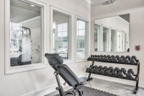 A room with a mirror, a bench of dumbbells and a stationary bike.