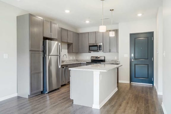 an open kitchen with stainless steel appliances, grey cabinets, and granite counter tops