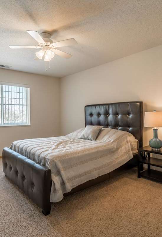 A bedroom with a bed, a nightstand, and a ceiling fan.