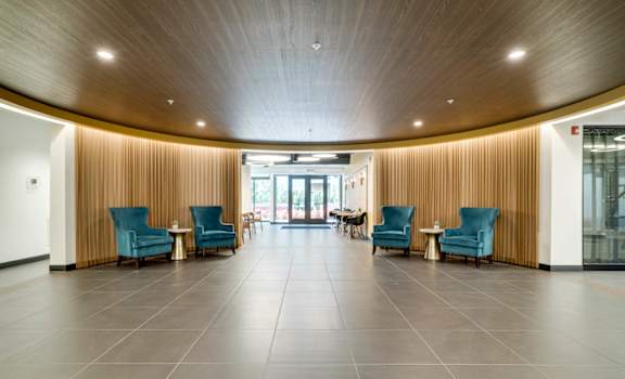 An open apartment lobby with blue chairs and a wooden ceiling.