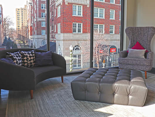 A grey sofa and a grey chair with a red pillow are in front of a window. at The Elle on Lockwood Apartments, Webster Groves, MO, 63119