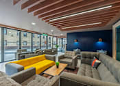 Thumbnail 7 of 8 - A modern lounge area with wooden slats on the ceiling and grey couches.