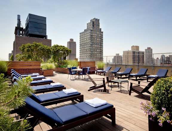 A rooftop patio with blue lounge chairs and wooden flooring.