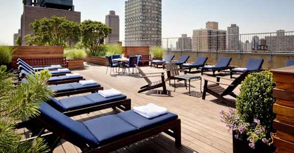 A rooftop patio with blue lounge chairs and wooden flooring.