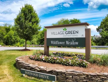 a stone retaining wall with flowers in front of a sign that says village green wildflower me