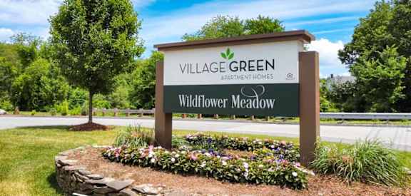 a stone retaining wall with flowers in front of a sign that says village green wildflower me