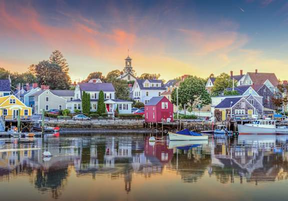 A serene harbor scene with boats docked and buildings along the water's edge.
