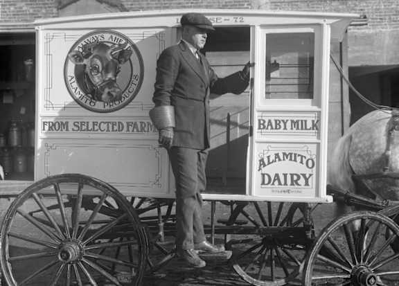 A man stands next to a wagon with a sign that reads "Alamito Dairy."