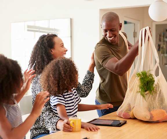 A man is holding a bag with vegetables in it while two children look on.